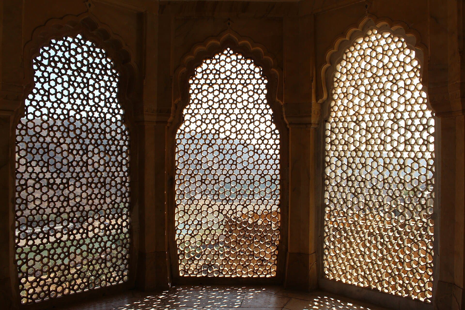 Sunlight passing through three pierced stone jali screens set in cusped arches.